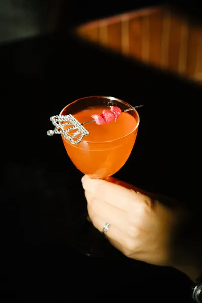 A guest holding a coral cocktail in a coupe glass at Čin Čin bar, Vračar