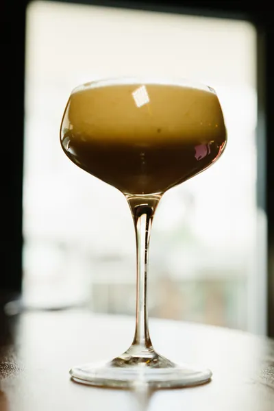 A coffee-coloured author cocktail in a coupe glass by the window