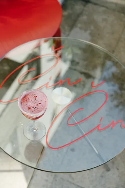 A pink sparkling cocktail on a glass table with the Čin Čin logo, Belgrade
